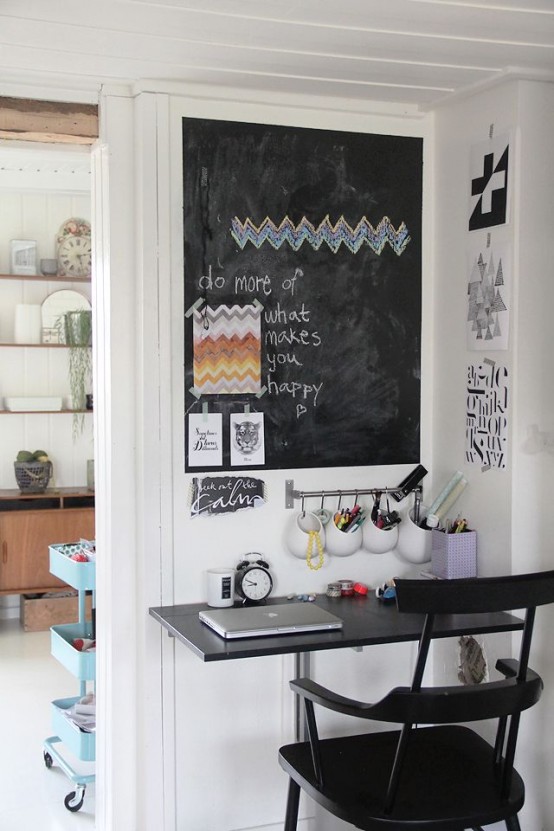 a tiny working studying space with a small wall-mounted desk, a black chair, a chalkboard and railing with various organizers is a lovely space