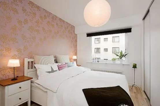 a small catchy bedroom with a peachy wallpaper wall, stylish furniture and black touches for some drama