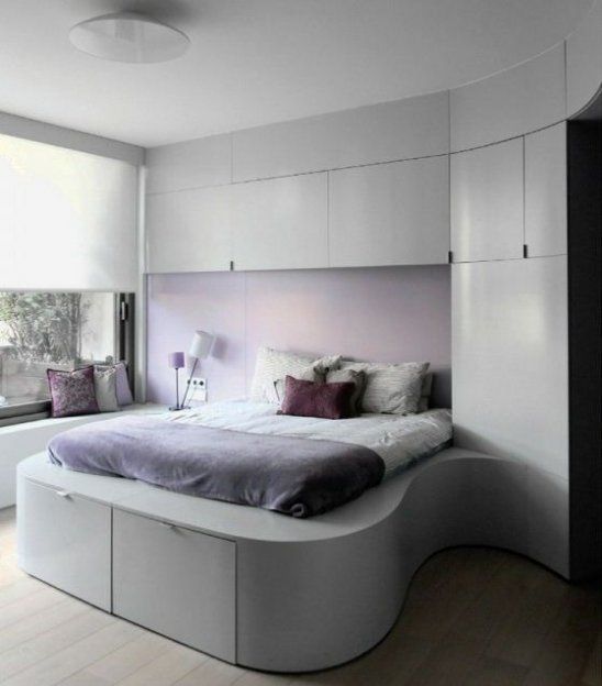a tiny minimalist bedroom with sleek neutral storage units and a storage bed, a purple wall and bright pillows plus shades