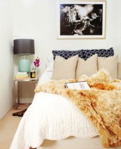 a small bright bedroom with an upholstered bed, bright bedding, a cool artwork and a nightstand with a lamp