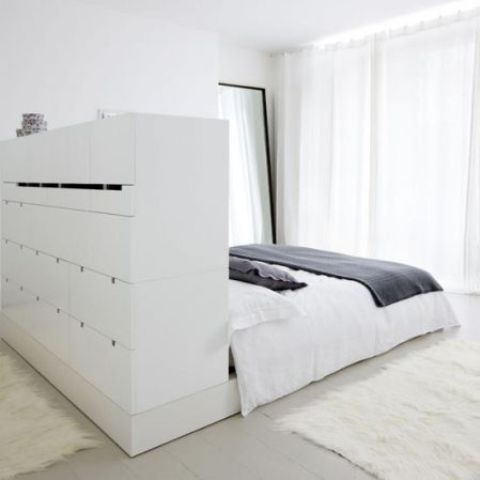 a large white minimalist bed with a storage headboard with lots of drawers that doubles as a space divider is brilliant