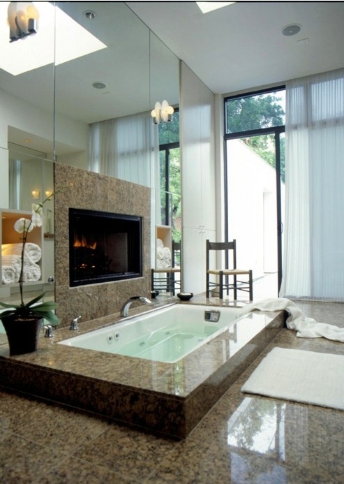 A modern bathroom with a mirror wall, a sunken bathtub clad with tiles, a built in fireplace and a glazed wall with a curtain