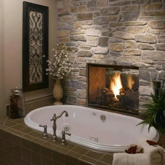 A vintage bathroom with a stone wall with a built in fireplace, a bathtub clad with green tiles and some greenery