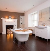 a contrasting bathroom with a faux fireplace with lights, a clawfoot bathtub, white storage units and shelves and a mirror