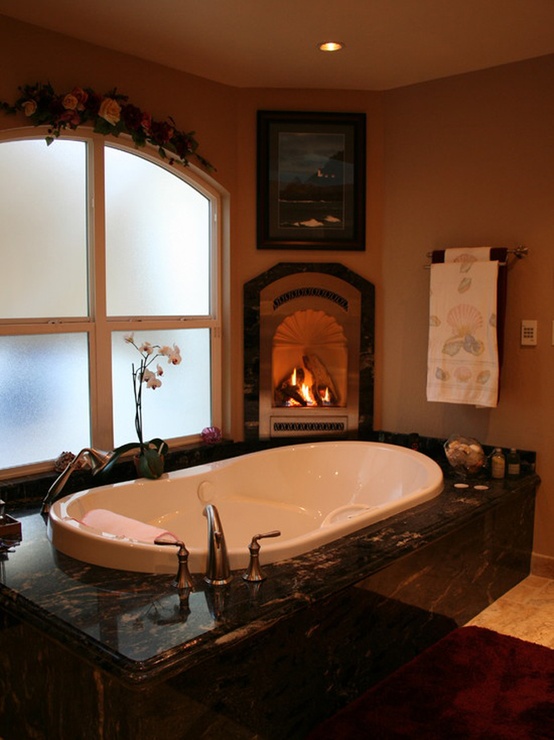 A vintage earth toned bathroom with a sunken bathtub, a built in fireplace, an arched window with frosted glass