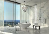 a white marble bathroom with a glazed wall, a large shower space, an oval bathtub and a mother of pearl chandelier and a glass fireplace