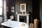 a moody black bathroom with a vintage fireplace and a mantel, a gallery wall, a black vintage bathtub and baskets for storage