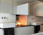 a modern neutral bathroom with a mirror cabinet, a fireplace, a vanity with sinks and dark towels