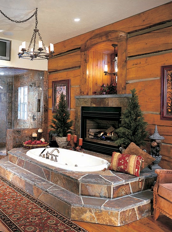 a rustic bathroom clad with wood, with a shower space, a sunken bathtub clad with stone, a fireplace , potted Christmas trees and pillows
