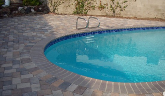 a blue oval pool with a beige stone deck and a bit of greenery around are a perfect combo that you may rock for your backyard - nothing else is needed