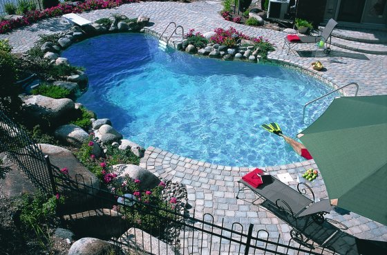 A kidney shaped pool with a whitewashed stone deck, large rocks, greenery and bright blooms around is a cool space to refreshing on a hot day