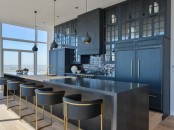 a matte black kitchen with sleek and profiled cabinets, a large kitchen island with a waterfall backsplash, black stools and pendant lamps