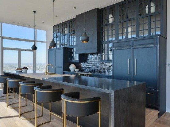 a matte black kitchen with sleek and profiled cabinets, a large kitchen island with a waterfall backsplash, black stools and pendant lamps