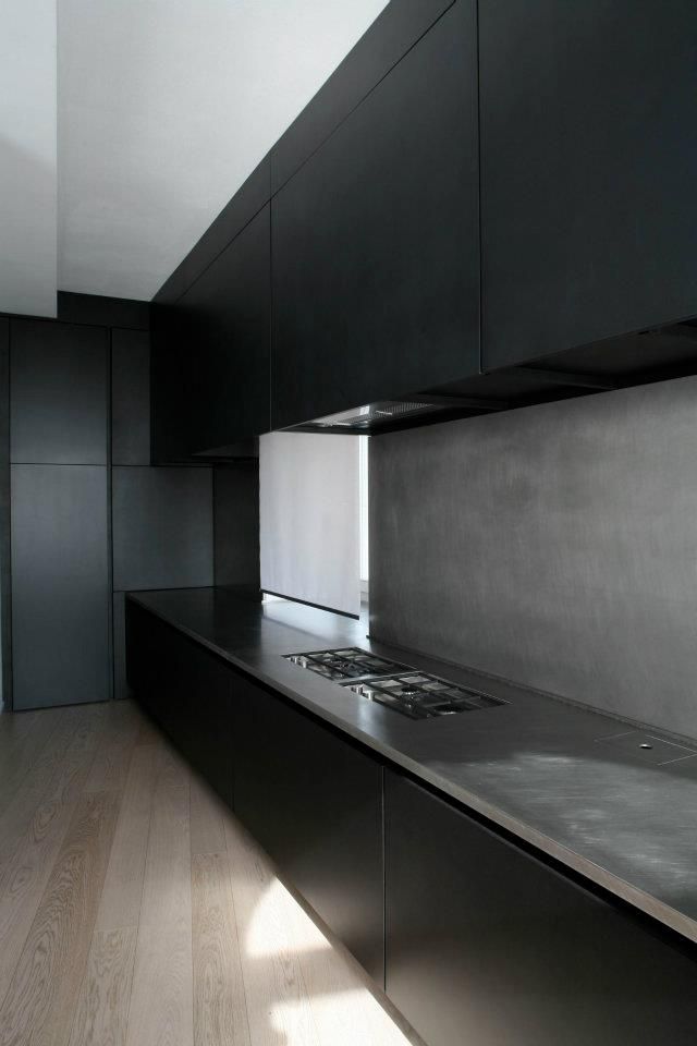 A matte black kitchen with a concrete backsplash and countertops and everything hidden plus a window in the backsplash to enliven the space a little bit