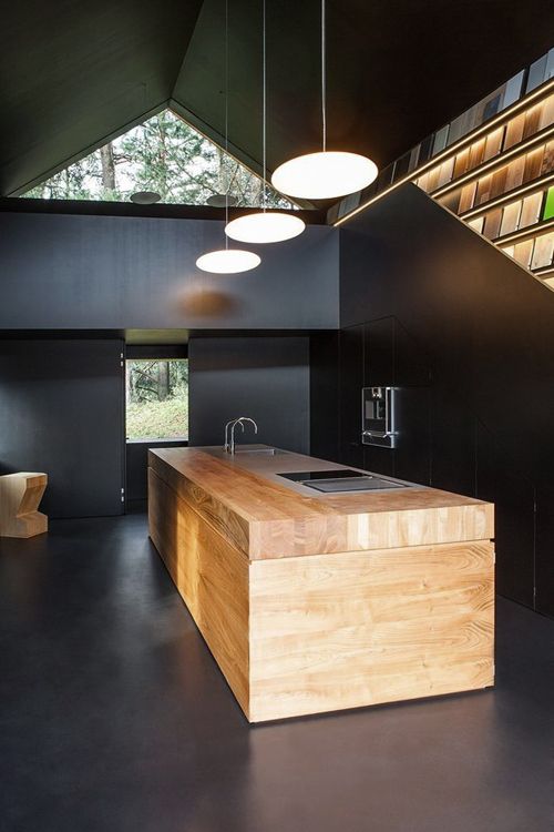 A catchy minimalist black kitchen with a light stained kitchen island that refreshes the space and pendant lamps over it