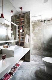 a contemporary industrial bathroom done with concrete, a white vanity with a sink, a shower space, a mirror and touches of red for a bold look