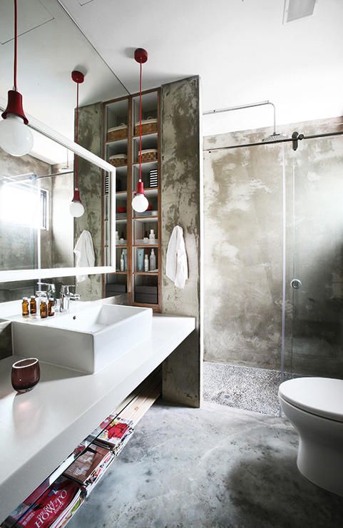 a contemporary industrial bathroom done with concrete, a white vanity with a sink, a shower space, a mirror and touches of red for a bold look