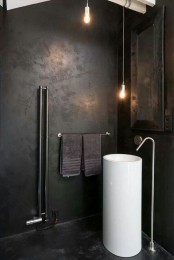a dark industrial bathroom with metal clad walls, a mirror in a wooden frame, pendant lamps and a free-standing sink
