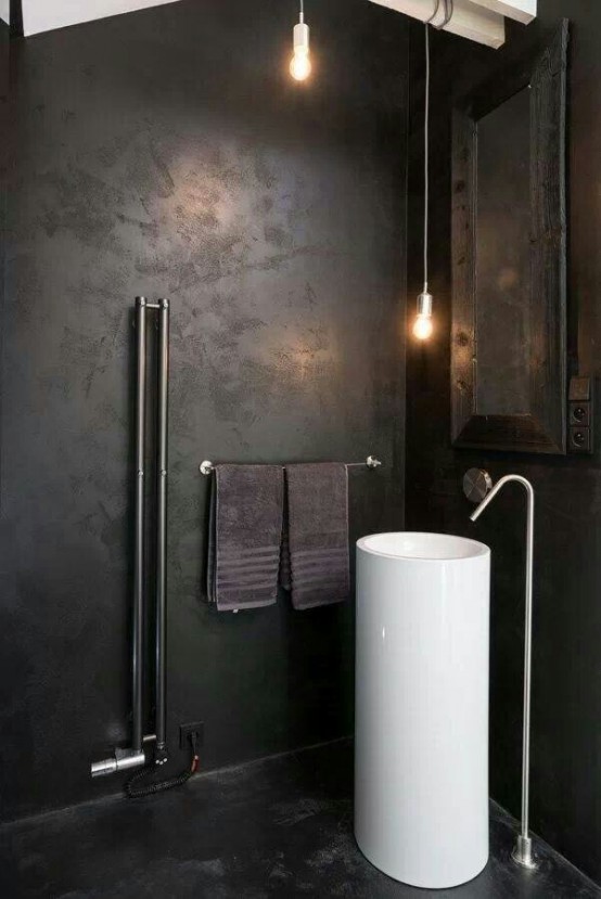 a dark industrial bathroom with metal clad walls, a mirror in a wooden frame, pendant lamps and a free-standing sink