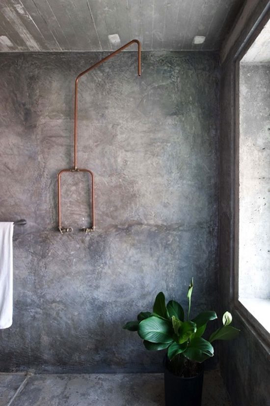 a modern industrial bathroom with concrete walls and a floor, an exposed copper pipe and potted plants is a chic and functional space