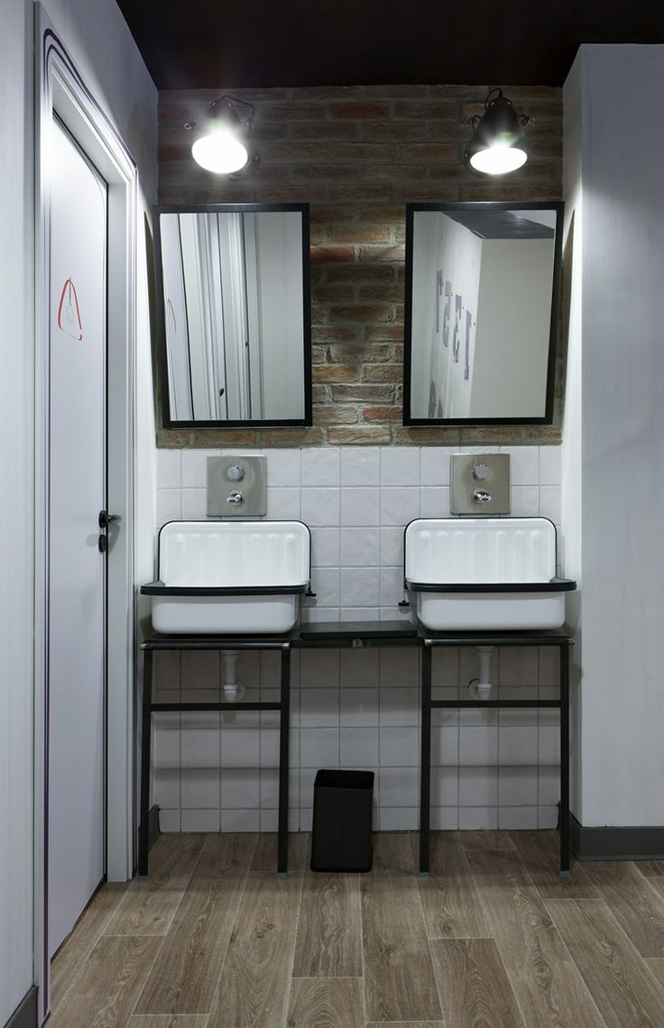 A modern industrial bathroom with white tiles, a brick wall, a wooden floor, vintage sinks on a stand and a duo of mirrors
