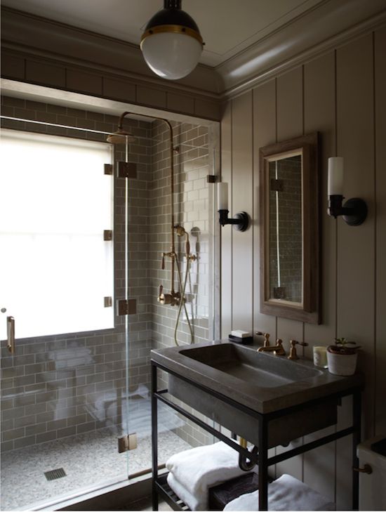 a moody vintage bathroom with industrial touches, grey tile and beadboard walls, a stone sink on a stand, pendant lamps and a window in the shower