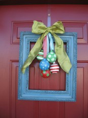 a front door Christmas wreath made of a blue frame with colorful ornaments and a green silk bow is a whimsy and cool idea