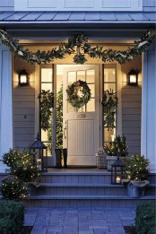 natural front door Christmas decor with an evergreen garland and posies, a wreath and evergreens in buckets with lights