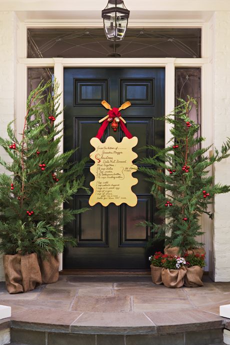 a Christmas front door with an artwork with song lyrics, Christmas trees with red ornaments and blooms in burlap
