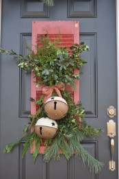a vintage Christmas door decoration with a red shutter, greenery and berries and oversized bells