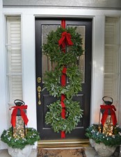 chic Christmas front door styling with evergreen wreaths and a red ribbon, lanterns with lights and red bows plus evergreens