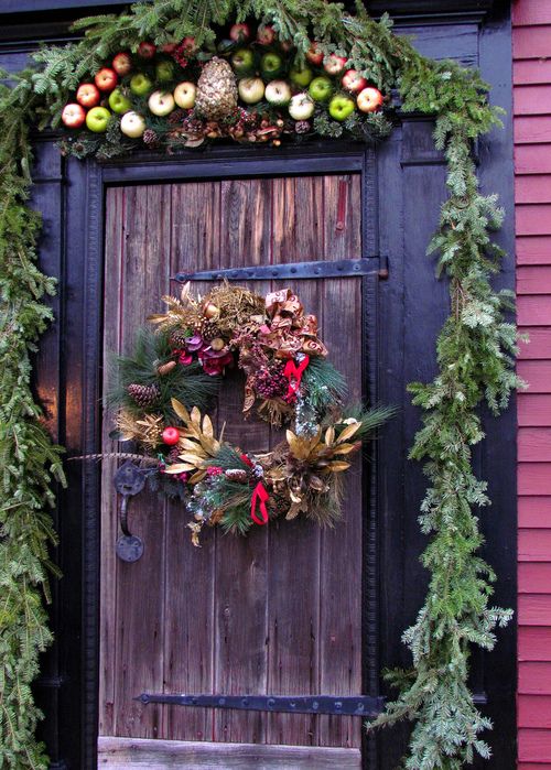 Christmas front door decor with an evergreen garland, pinecones, apples and a quirky wreath with pinecones, apples, dried leaves and berries