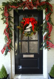 chic front door Christmas styling with an evergreen garland with pinecones and apples, plaid ribbons and skates with a bow instead of a wreath
