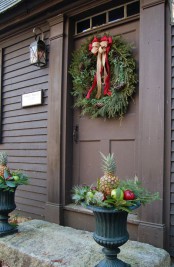 creative front door styling with an evergreen wreath with pinecones and bows plus urns with pineapples and fruits for a whimsy touch