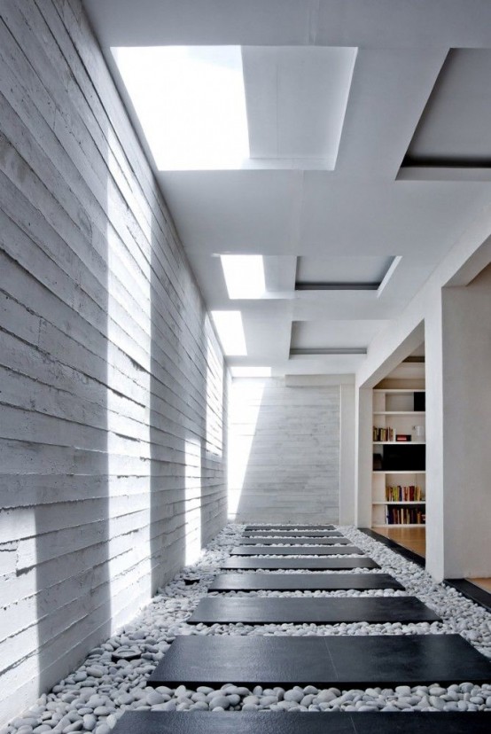 a minimalist indoor courtyard with white pebbles and black planks over them plus skylights is a fresh design solution