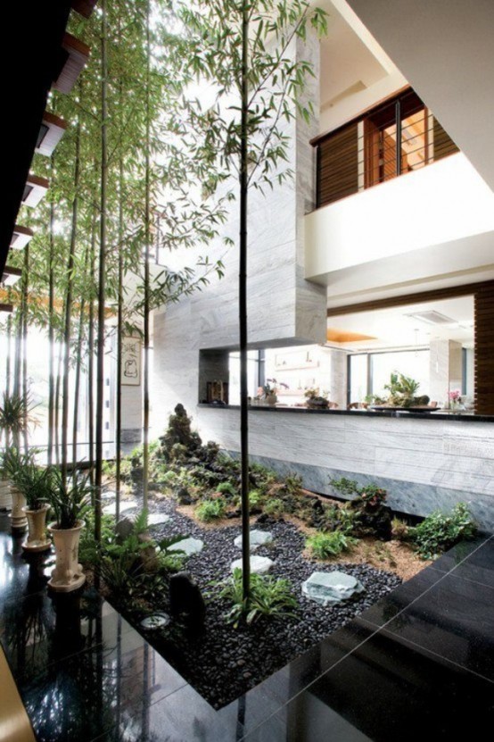 a spectacular indoor courtyard with black pebbles, growing and potted greenery and some tall trees that highlight the double-height ceilings
