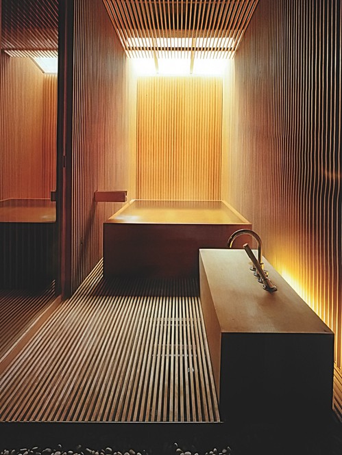 a Japanese minimalist bathroom clad with light stained wooden slabs, with a wooden bathtub nand a creative vanity with a sink plus a skylight