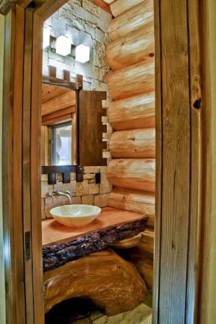 a wooden bathroom clad with wooden logs, a rough wood vanity and a stone accent wall is a lovely idea to rock