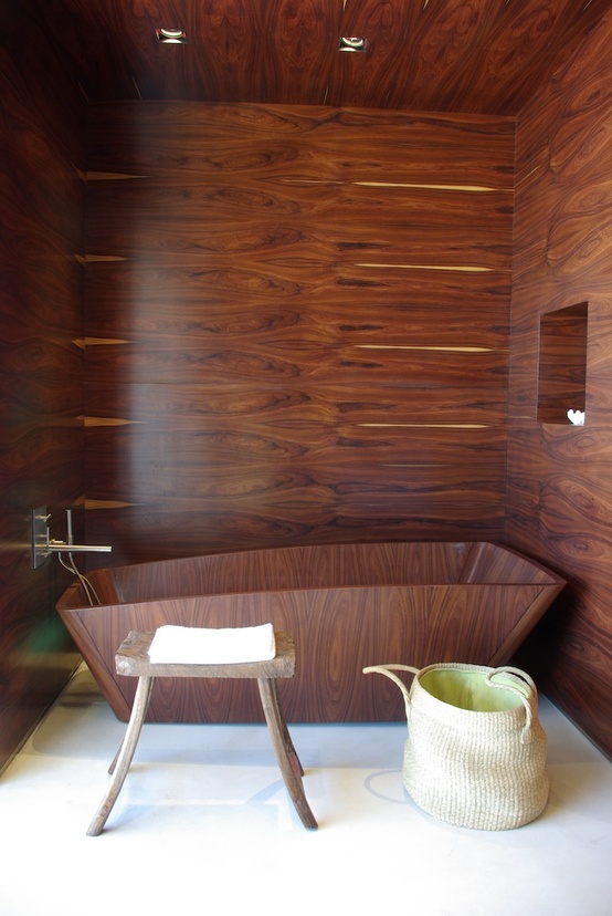 a rich stained wood clad bathroom with a matching bathtub, a small stool and a basket plus a niche for storage