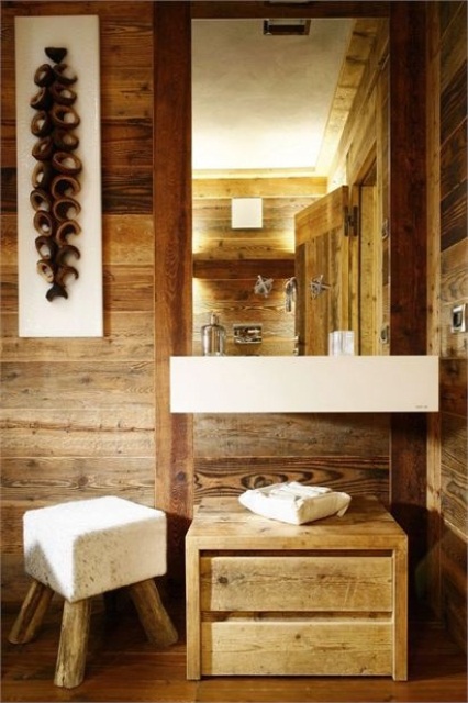 A contemporary bathroom clad with wood, with a mirror in a wooden frame, a wall mounted sink, a wooden storage unit and a cool cube stool