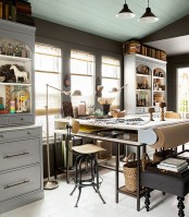 an eclectic home office done in neutrals, a tall desk, bookcases and a black ottoman