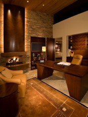 an elegant home office with a faux stone wall, rich stained wooden furniture and a fireplace, a rug and leather chairs