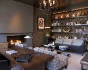 a moody home office with a concrete fireplace, a shiny wlal with open shelves, a rich stained wooden desk, catchy lamps and upholstered furniture