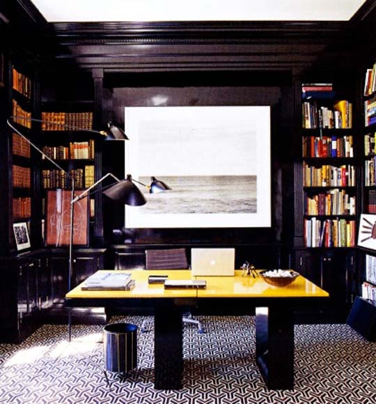 An elegant moody home office with black walls and built in bookcases, a black and gold desk plus a mosaic floor
