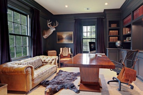 a refined moody home office with black walls, built-in shelves, rich stained wooden furniture and a matching leather sofa