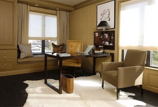 A modern home office done in tan and earthy shades, built in furniture, a black desk and a chair plus artworks
