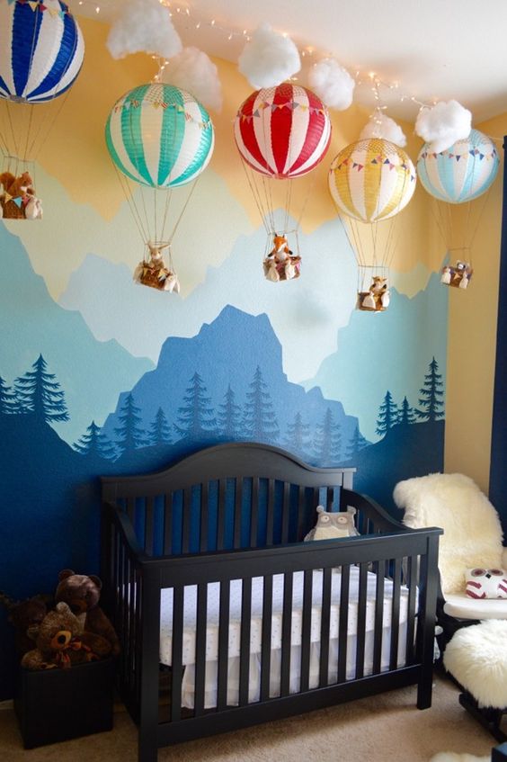 a lovely woodland nursery with a wall mural, a black crib, a white faux fur chair and lovely hot air balloons with various animals