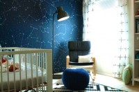 a galaxy-inspired nursery with a constellation accent wall, a white crib, a black chair and a navy pouf, a printed rug and a black floor lamp