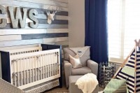 a rustic nursery with a reclaimed wood wall, neutral and contrasting furniture, a teepee and navy curtains