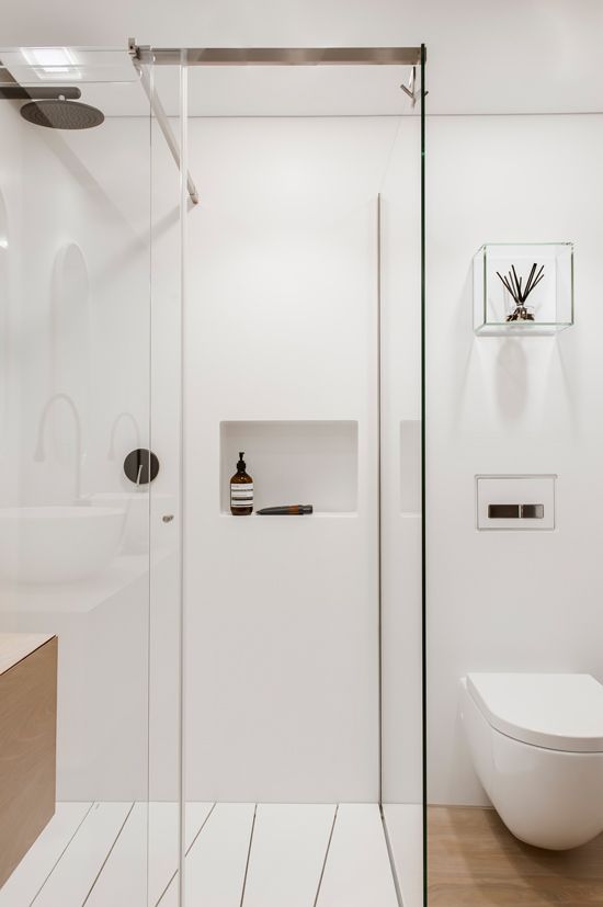 A small white minimalist bathroom with sleek walls, a wooden floor and vanity, built in storage and white appliances
